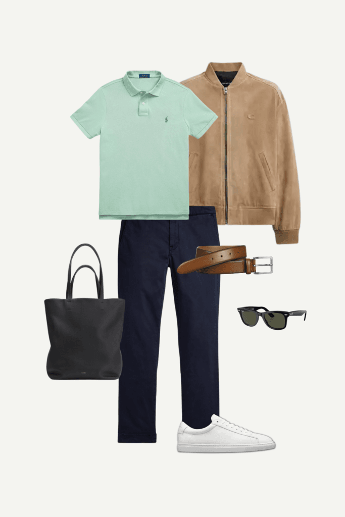 Flat lay of a men’s spring smart-casual outfit with a mint polo, suede jacket, navy chinos, white sneakers, black tote, sunglasses, and leather belt