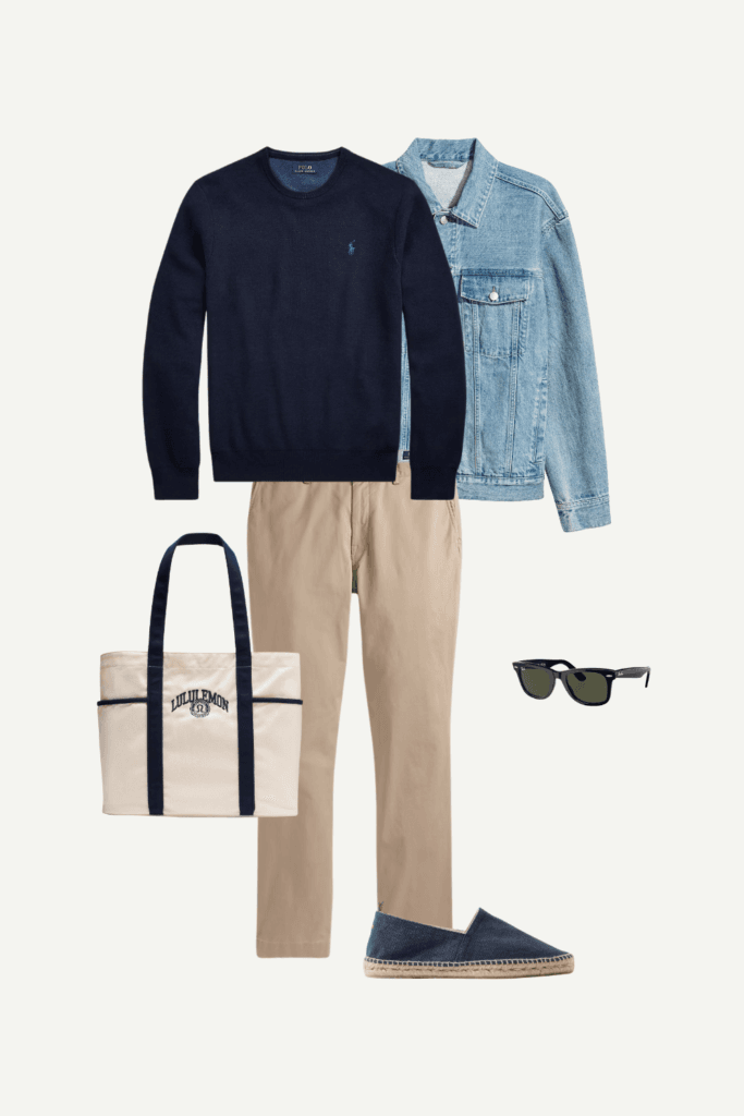 Flat lay of a men’s smart-casual spring outfit with a navy crewneck sweater, denim jacket, khaki chinos, navy espadrilles, black sunglasses, and a canvas tote bag.