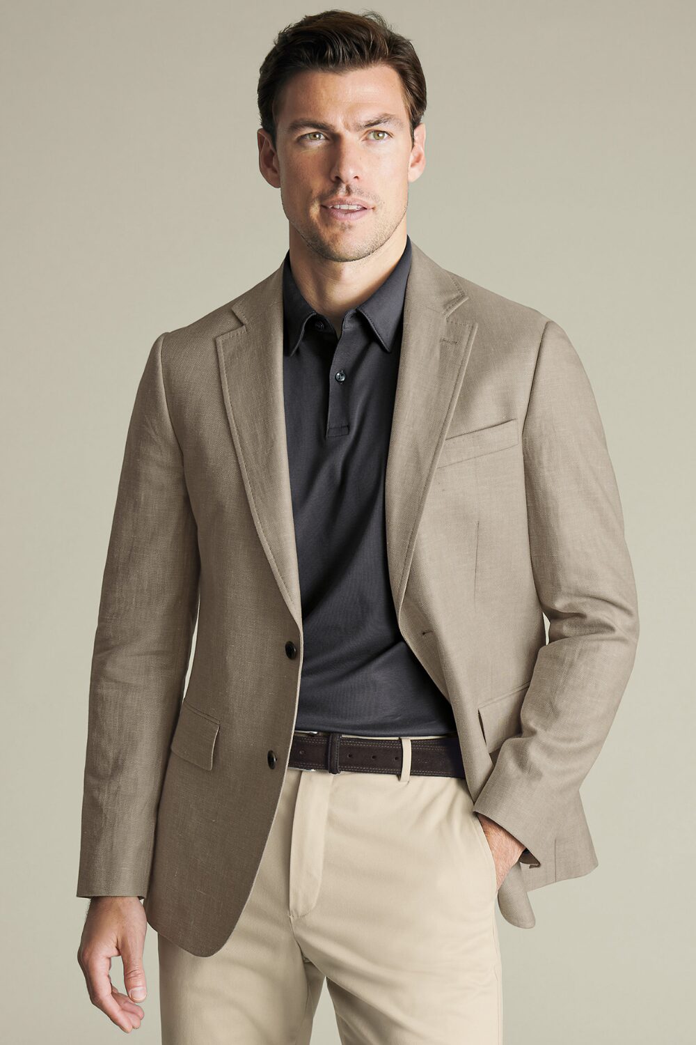 A man wearing a dark gray polo shirt, beige chinos, and a light brown blazer — a clean, casual smart casual outfit for warm-weather days.