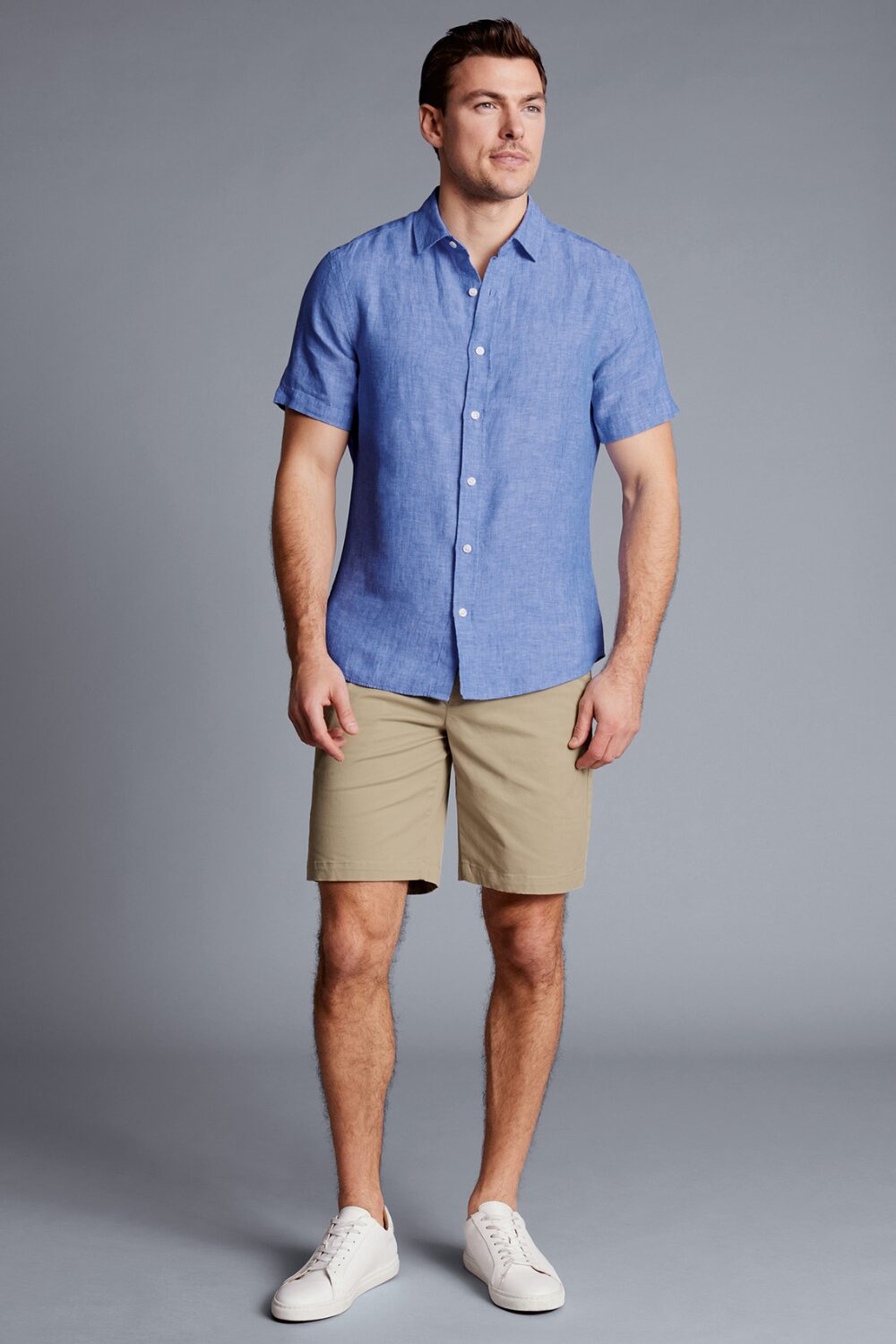 A man wearing a blue short-sleeve linen shirt and brown chino shorts — a relaxed, lightweight summer outfit.